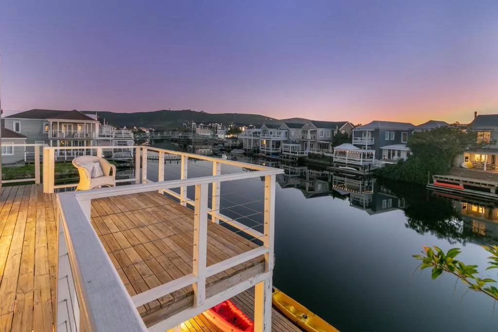 Wooden deck with white railings overlooking calm waterway and houses