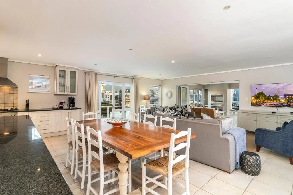 Wooden dining table with white chairs in modern open-plan kitchen and lounge