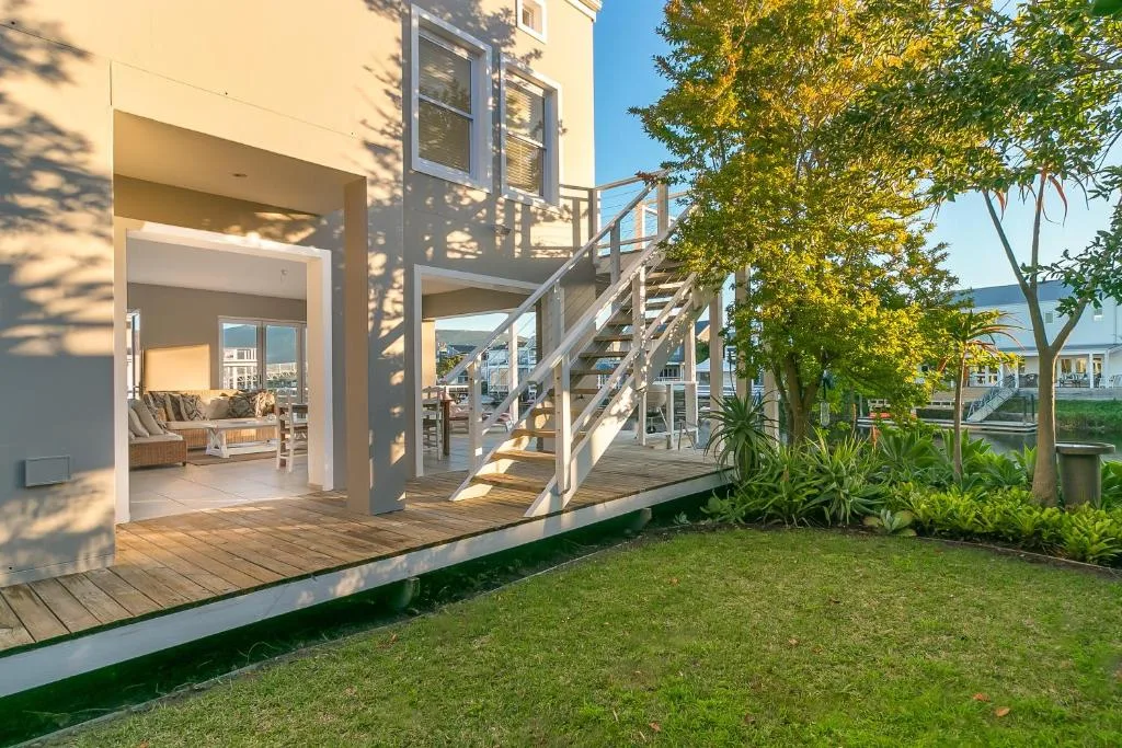 Modern waterfront villa with wooden deck, stairs, and manicured garden lawn
