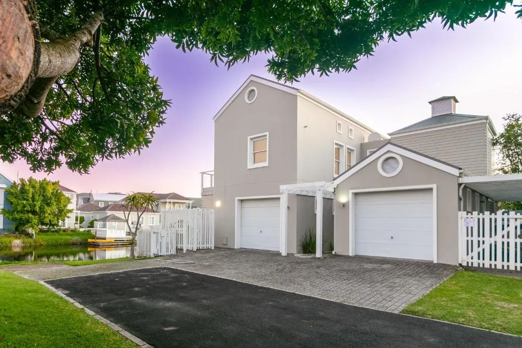 Modern beige villa with white garage doors and waterfront garden at dusk