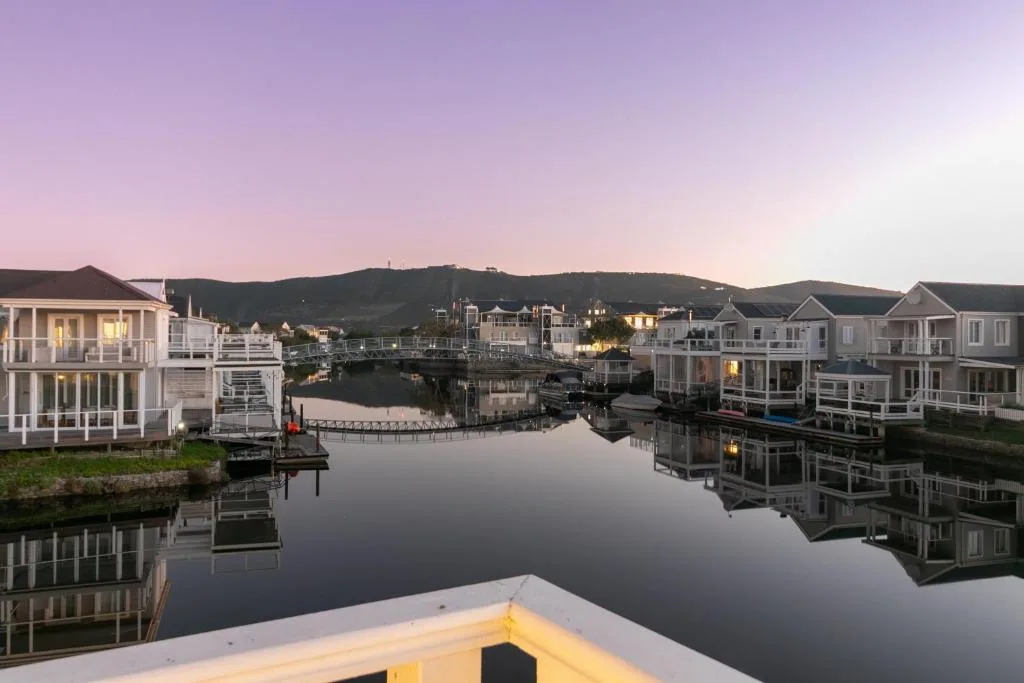 Tranquil waterfront village at dusk with mountain backdrop and reflected lights