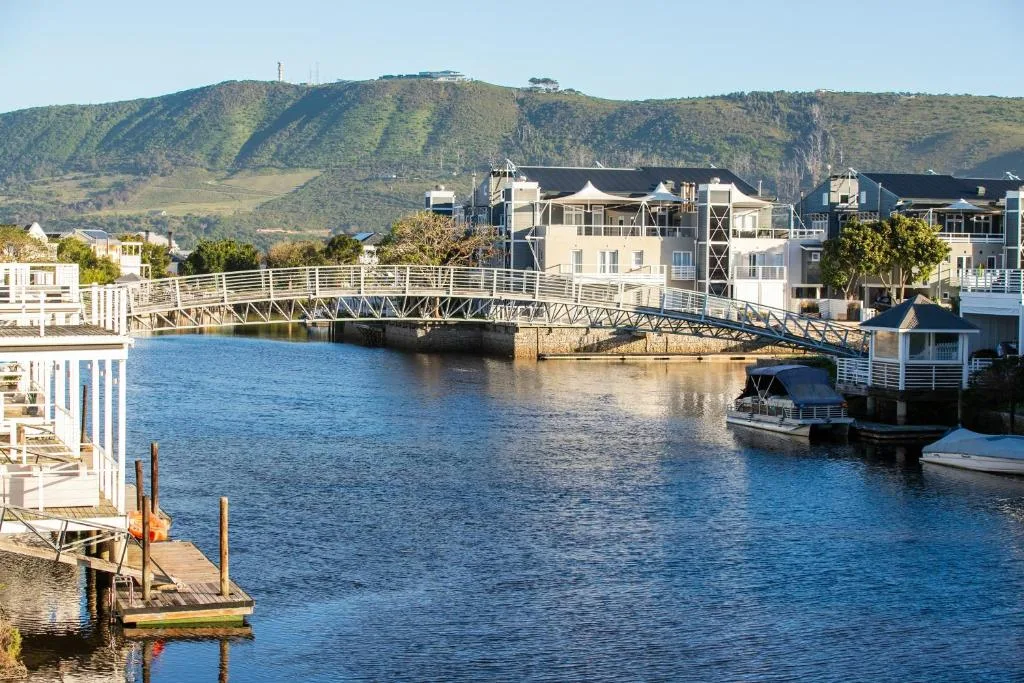 Waterfront village with bridge, boats, and green mountains backdrop