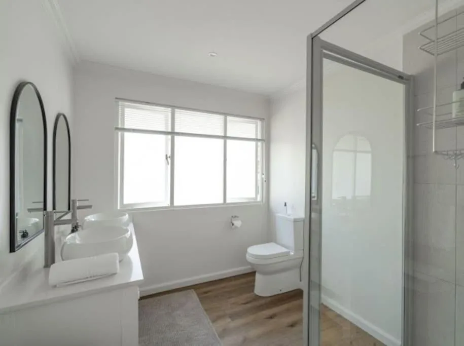 Modern bathroom with dual vanities, toilet, and walk-in shower enclosure