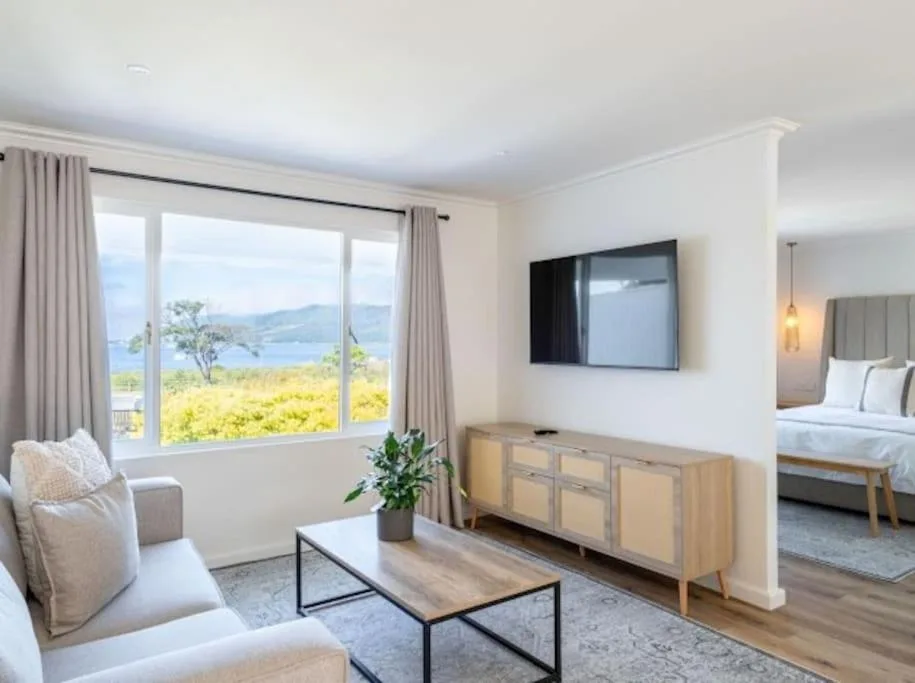 Bright lounge with TV, comfortable seating, and expansive lagoon views through large windows