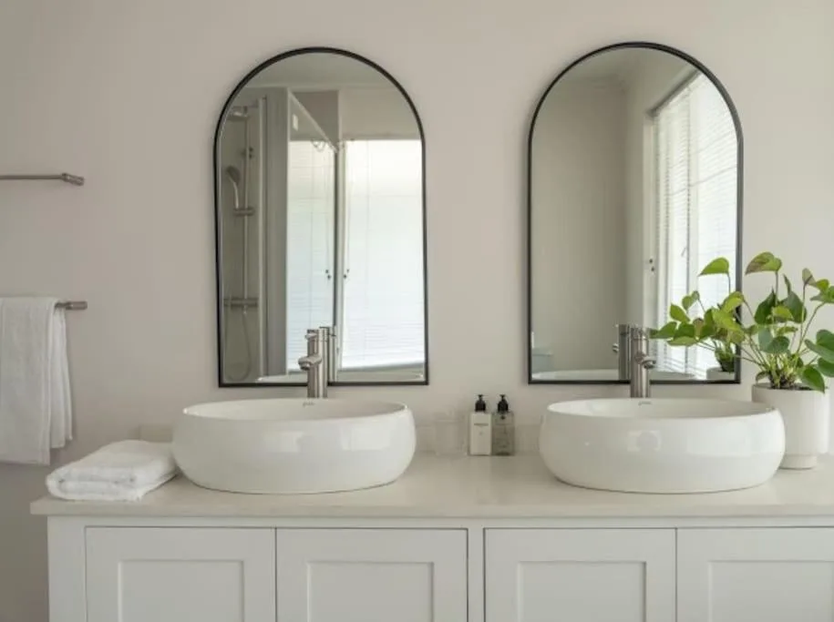 Modern dual vanity bathroom with round white sinks and arched mirrors