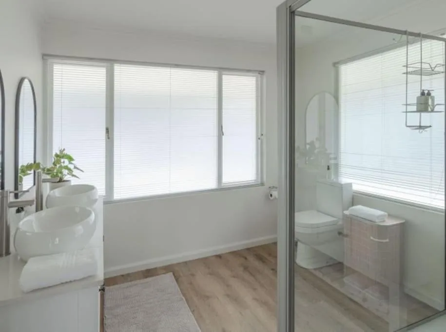 Modern bathroom with double vessel sinks, glass shower enclosure, and large windows