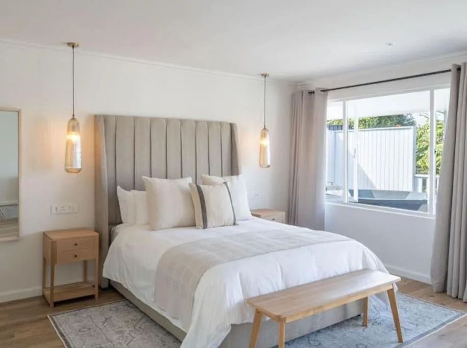 Bright modern bedroom with upholstered headboard, pendant lights, and lagoon views