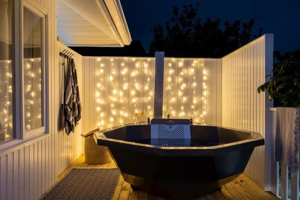 Outdoor bathtub with fairy lights on a wooden deck at dusk