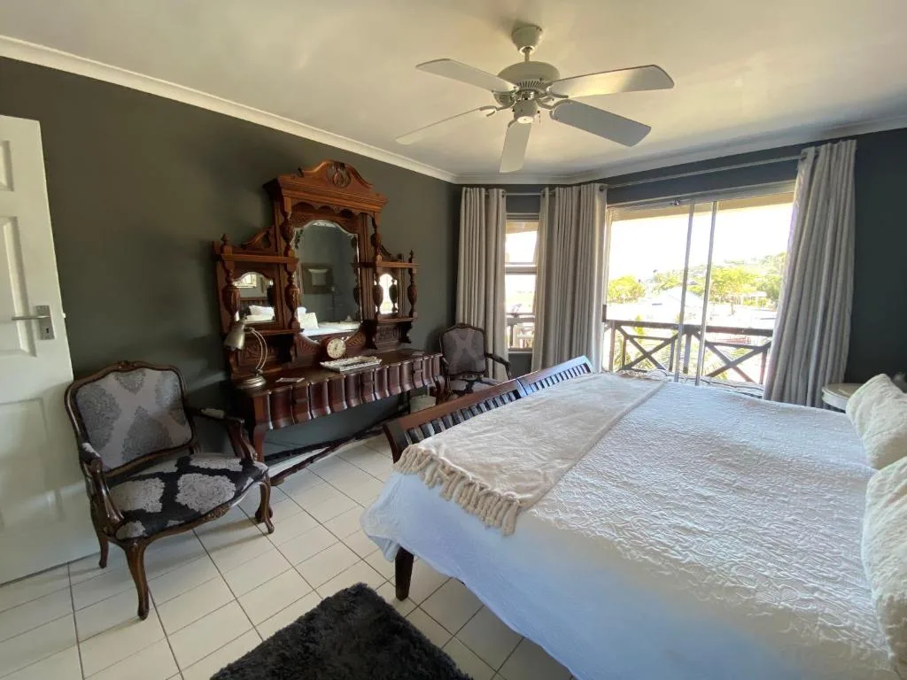 Spacious bedroom with queen bed, ornate wooden dresser, ceiling fan, and balcony access