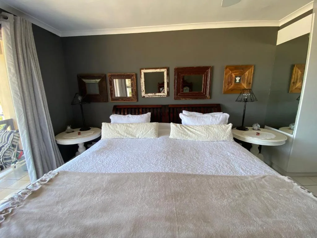 Spacious bedroom with double bed, sage green walls, decorative mirrors, bedside tables with lamps
