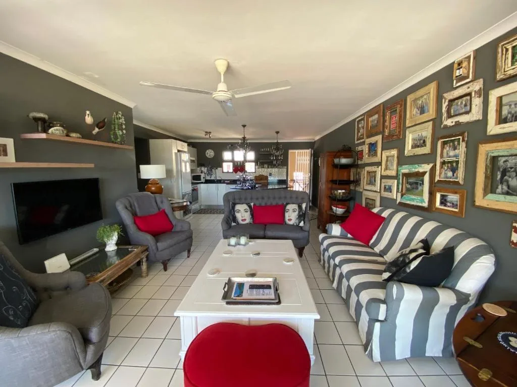 Open-plan lounge with grey walls, striped sofa, armchairs, TV, and gallery wall art