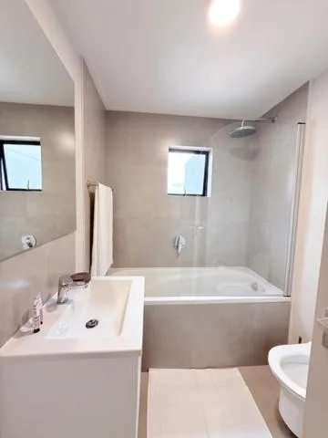 Modern bathroom with white vanity, bathtub, shower enclosure, and toilet