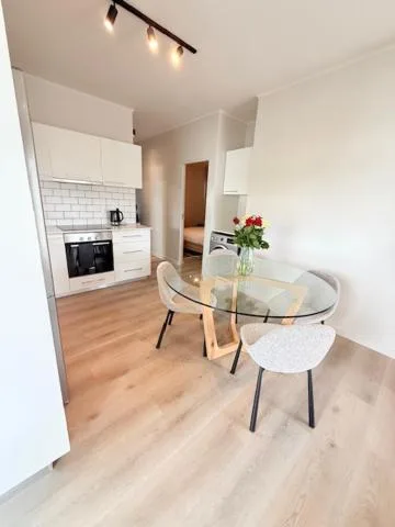 Modern dining area with glass table and white chairs near kitchen