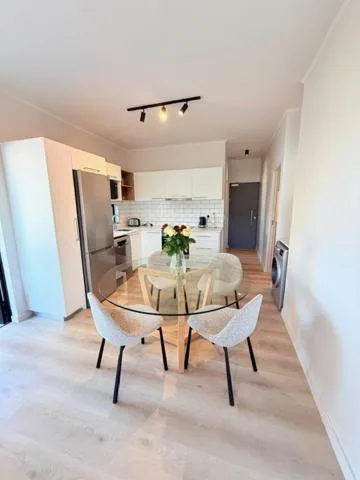 Modern dining area with round glass table and white chairs in open-plan kitchen