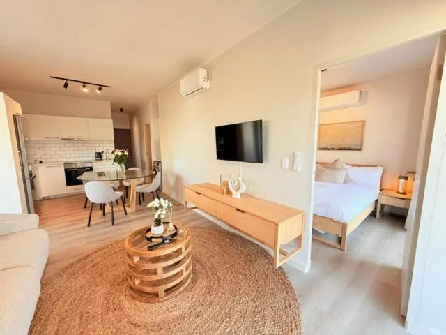 Open-plan lounge with wall-mounted TV, wooden furniture, and kitchen visible
