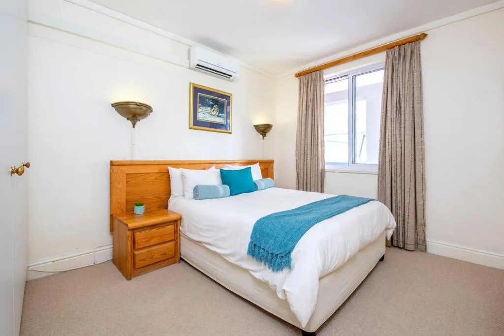 Spacious bedroom with wooden headboard, white bedding, turquoise accents, and large window