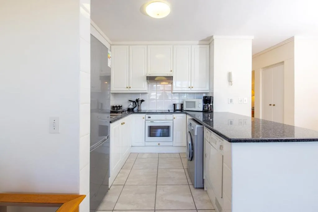 Modern white kitchen with granite counters, built-in appliances, and tiled flooring