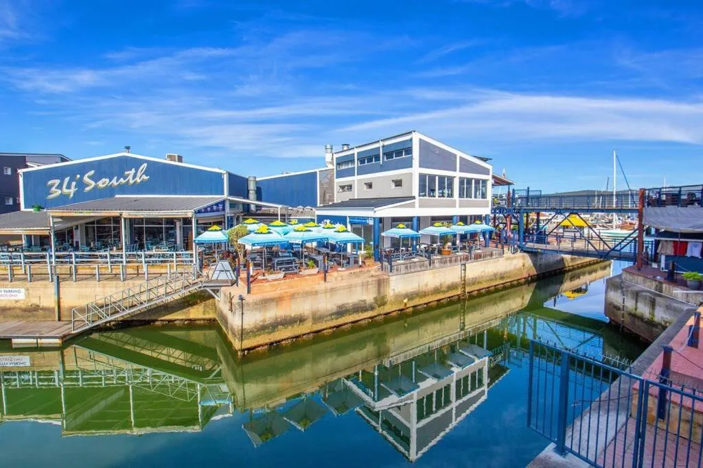 Waterfront restaurant and entertainment complex with blue umbrellas overlooking lagoon