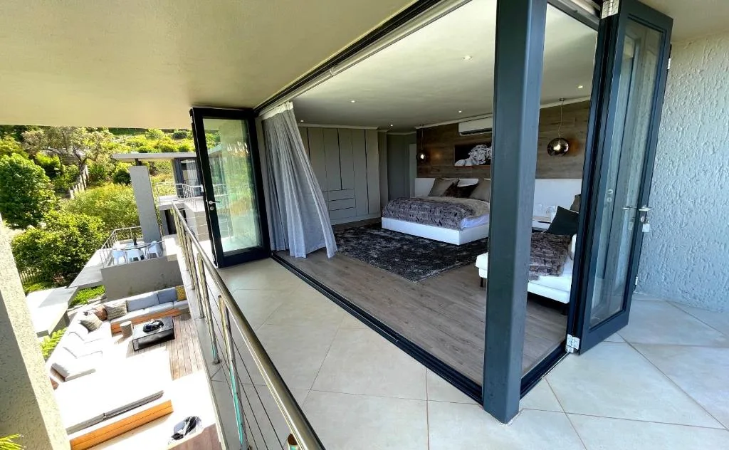 Modern bedroom with sliding glass doors opening to a private deck with garden views