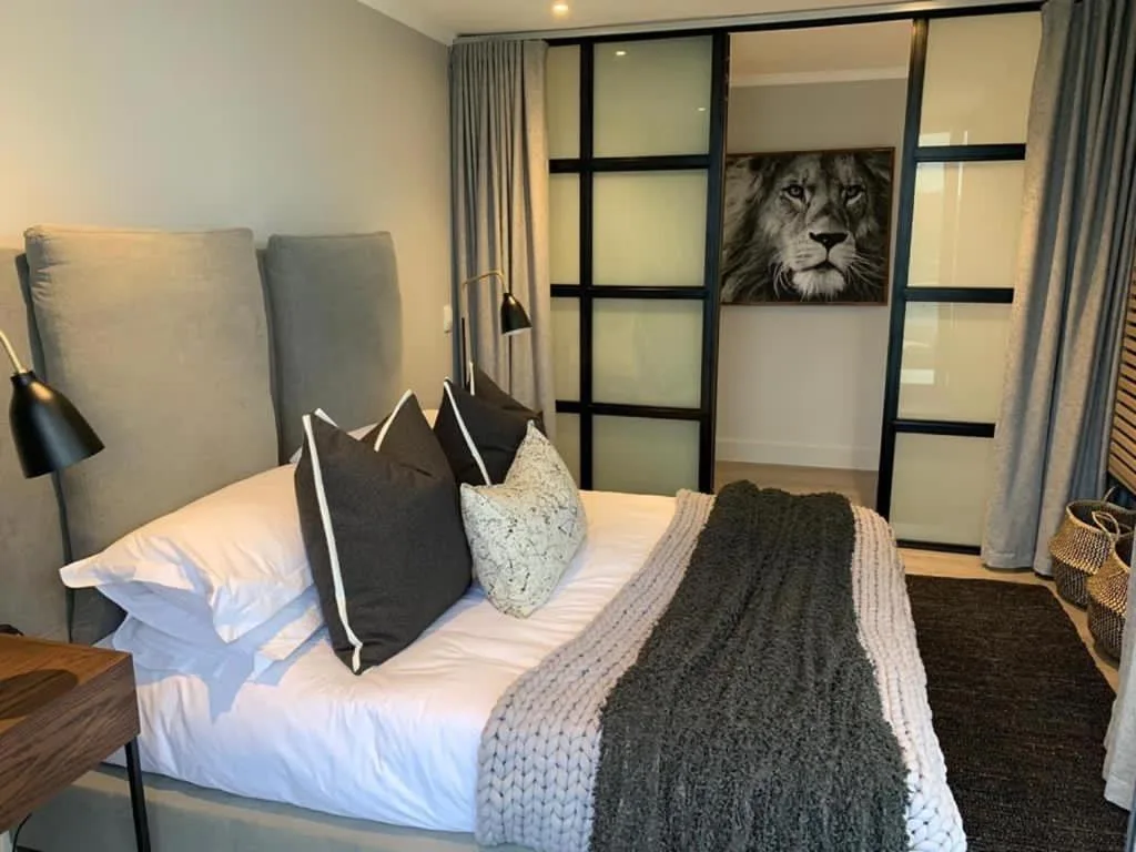 Modern bedroom with upholstered headboard, white bedding, decorative pillows, and lion artwork.