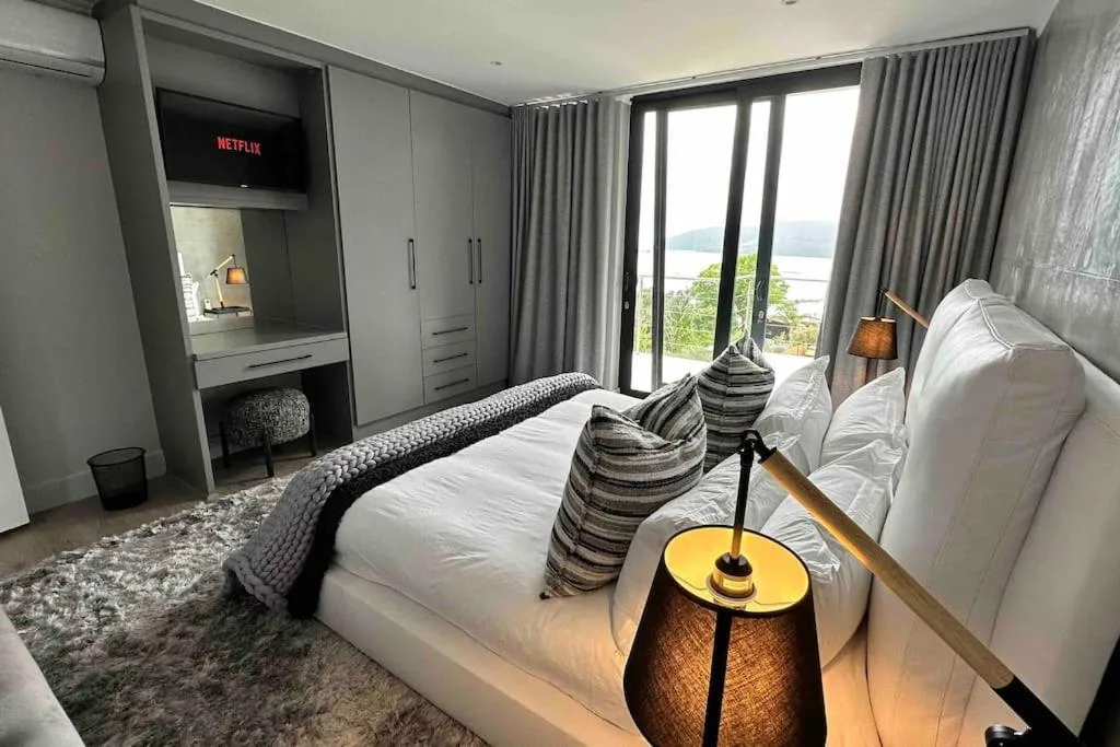 Modern bedroom with king bed, water views through glass doors, and entertainment setup