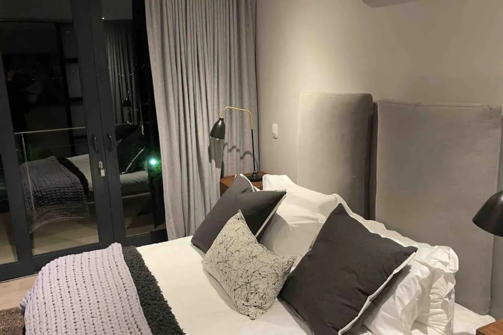 Modern bedroom with bed, pillows, reading lamp, and deck access.