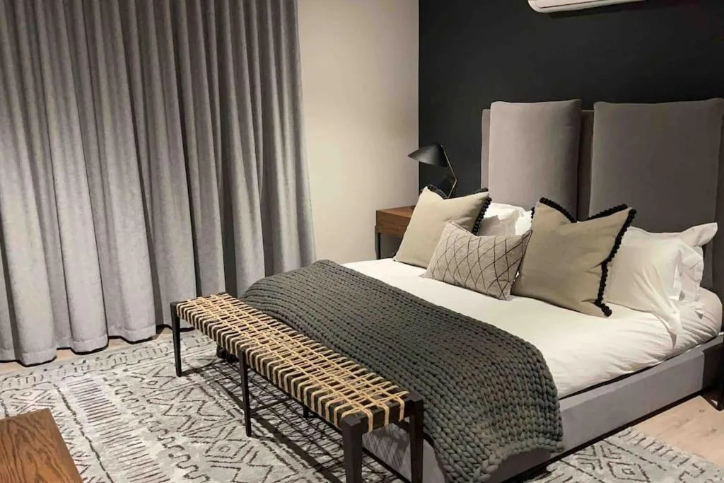 Modern bedroom with king bed, gray upholstered headboard, layered pillows, and sheer curtains