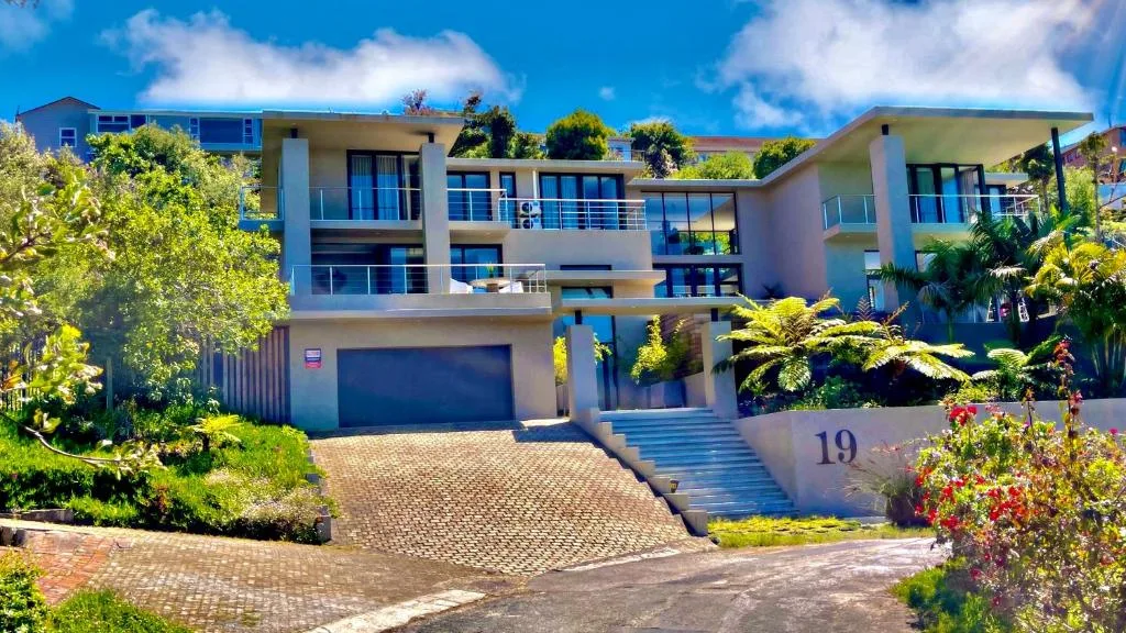 Modern three-story villa with cream facade, blue railings, garage, and manicured gardens