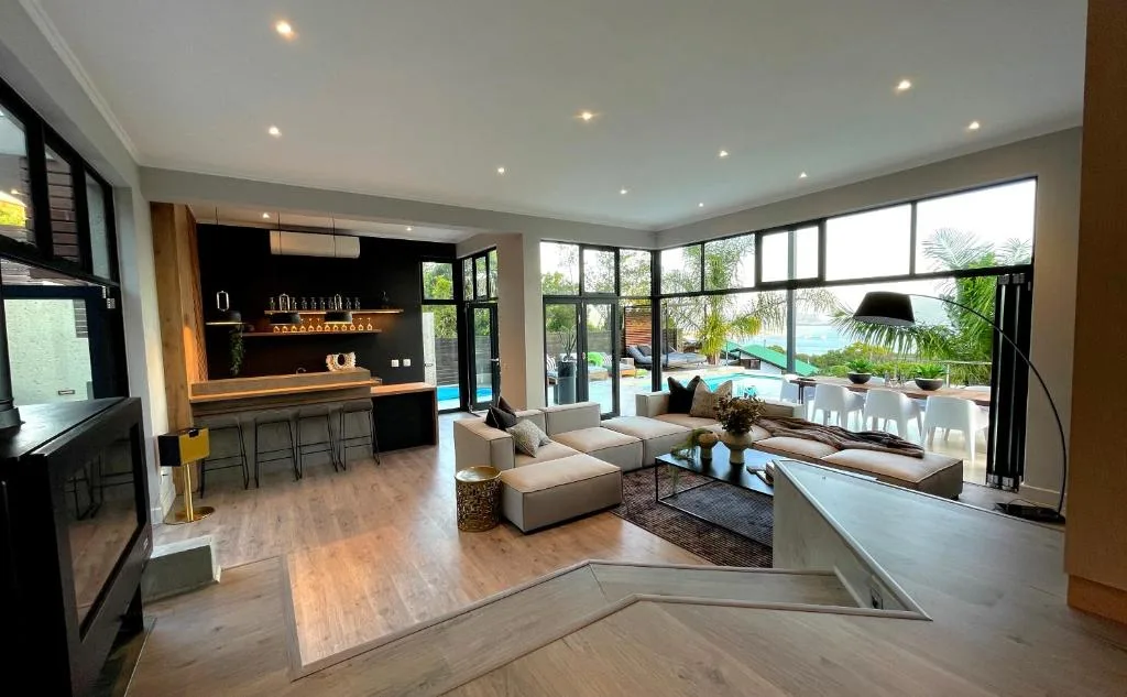 Modern living room with cream sofa, wood flooring, and large windows overlooking pool