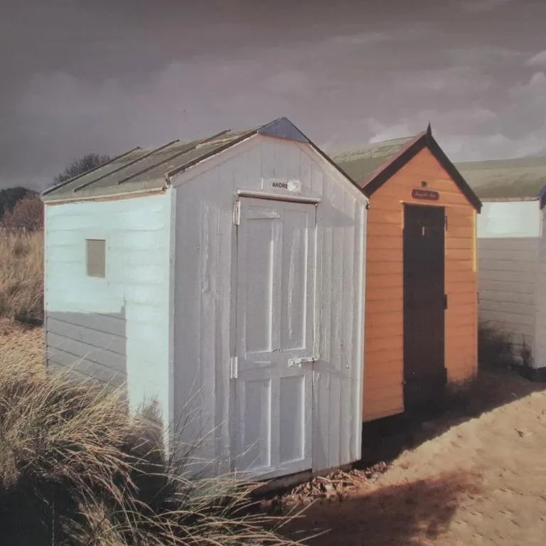 Colorful beach huts lined up on sandy shore with hills beyond