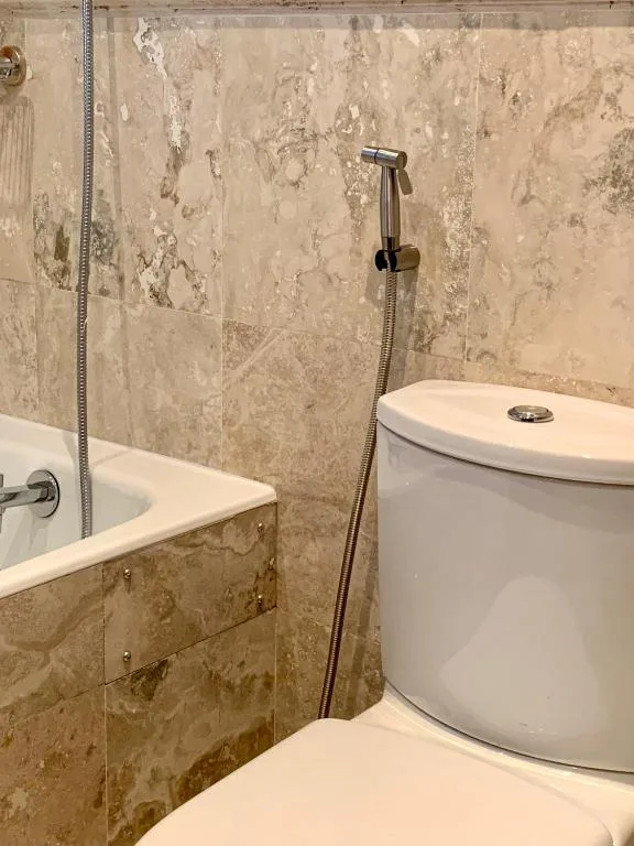 Modern bathroom with travertine tiles, white toilet, and hand shower fixture