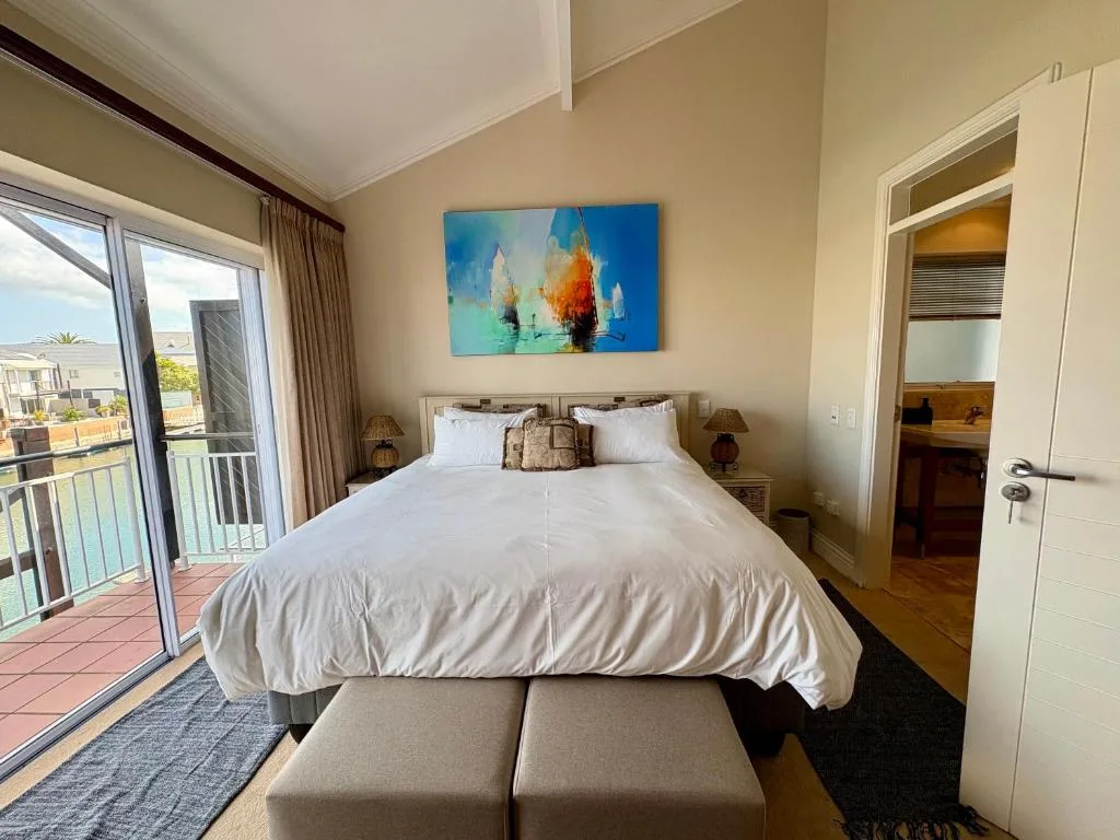 Bright bedroom with queen bed, white linens, and ocean view balcony access