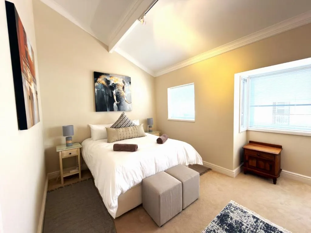 Bright bedroom with white bed, warm yellow walls, skylights, and modern decor
