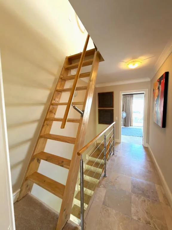 Wooden loft ladder leading to upper mezzanine in bright interior hallway
