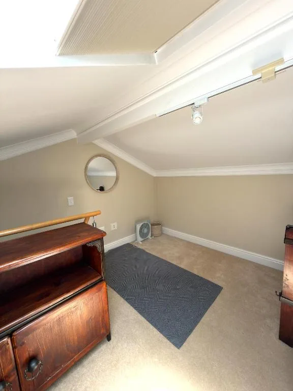 Attic room with wooden furniture, circular mirror, and neutral décor
