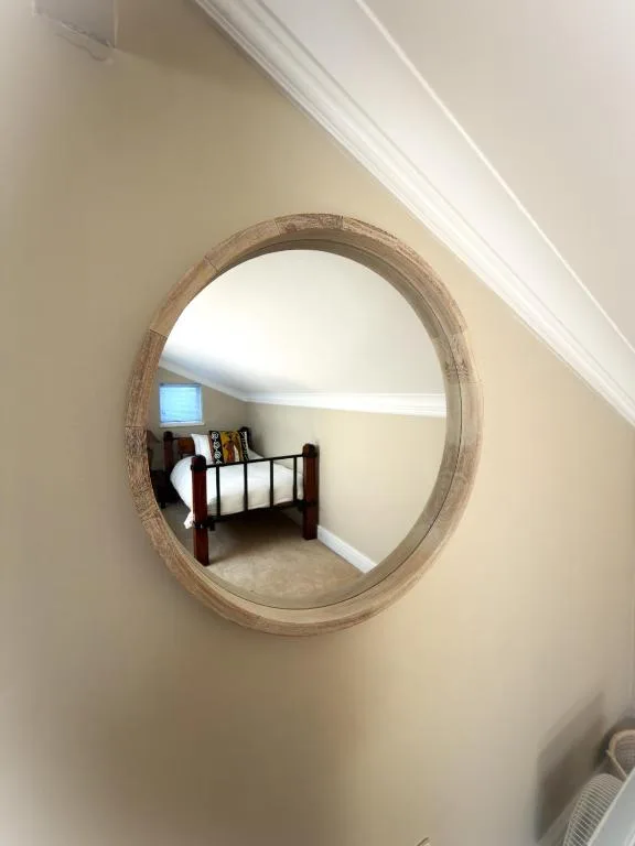 Wooden framed round mirror reflecting bedroom with iron bed frame