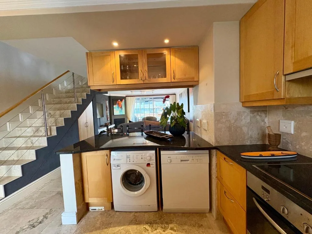 Open-plan kitchen with wooden cabinetry, dark countertops, washing machine and appliances