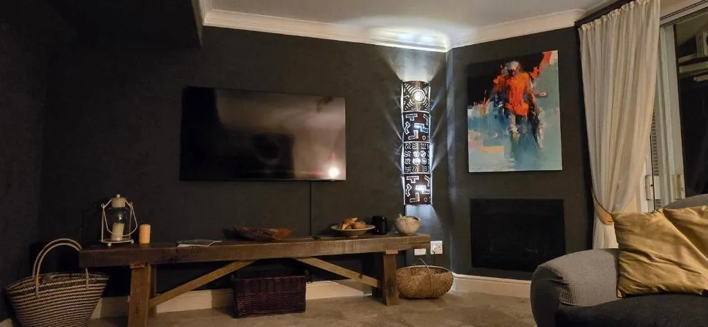 Modern lounge with dark walls, wooden desk, mounted TV, and contemporary artwork