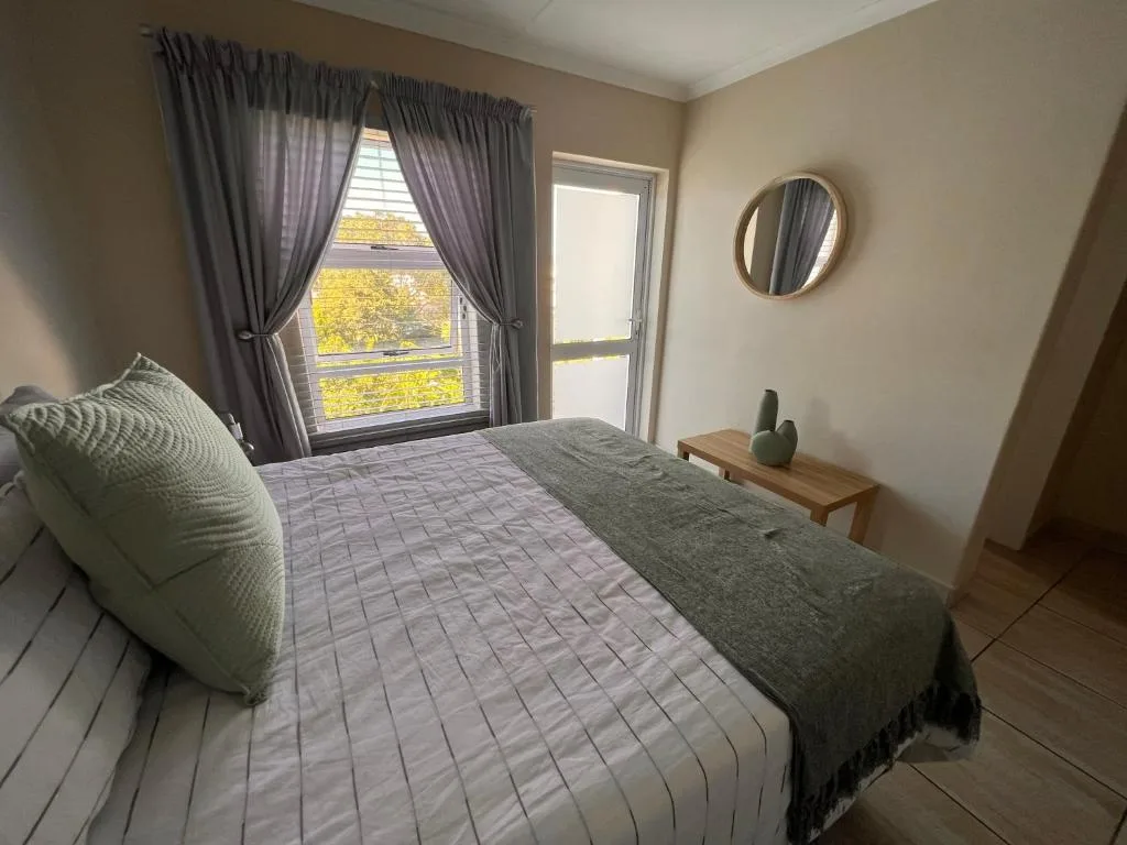 Bright bedroom with queen bed, round mirror, and garden views through large window