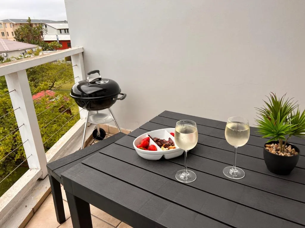 Outdoor deck table with braai grill, wine glasses, and garden views