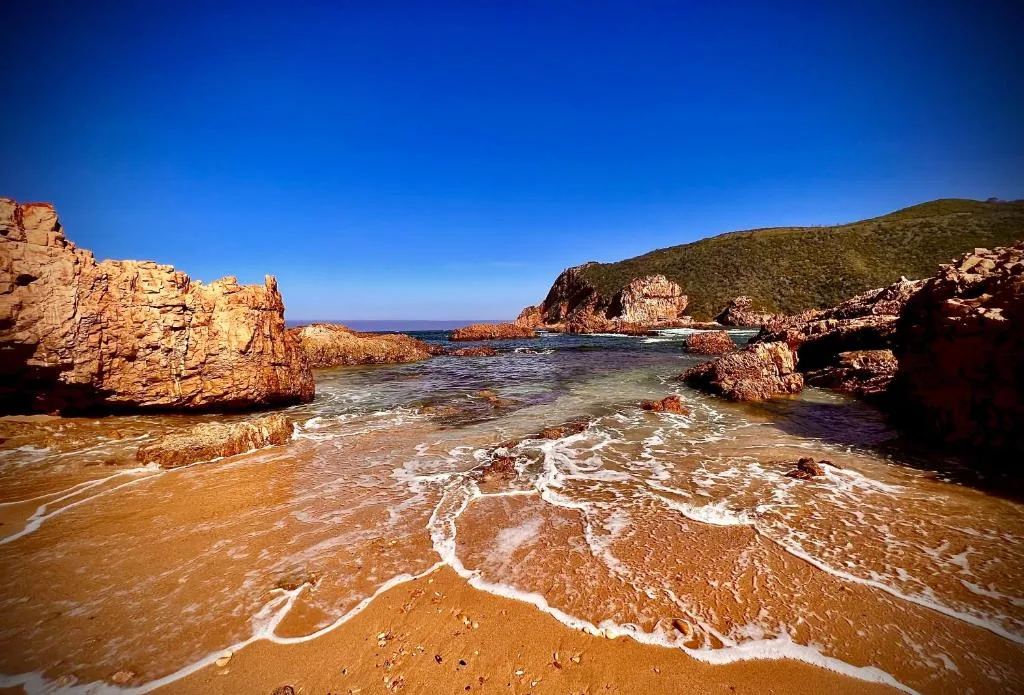 Scenic rocky cove with golden sand beach and clear blue ocean waters
