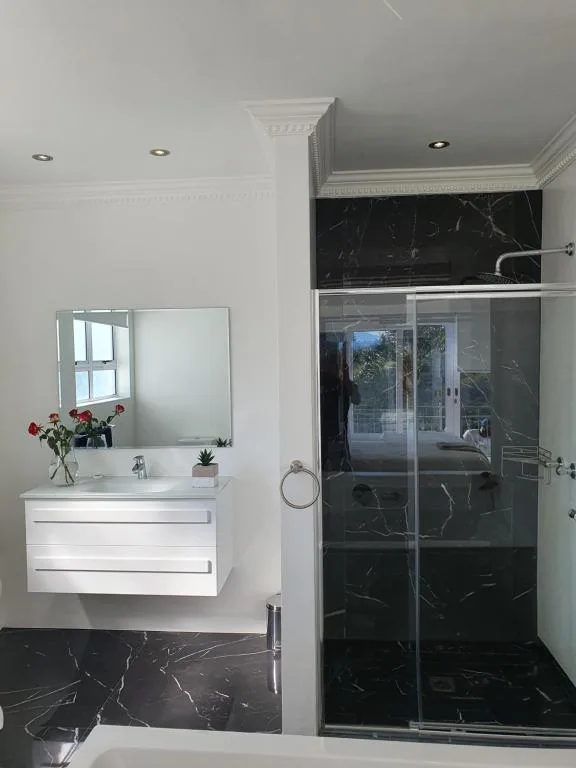 Modern bathroom with white vanity, mirror, and black marble shower enclosure