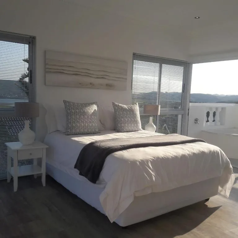 Bright bedroom with white bed, grey cushions, overlooking water view