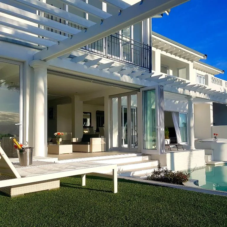 Modern white patio with pergola, lawn, and pool edge overlooking interior