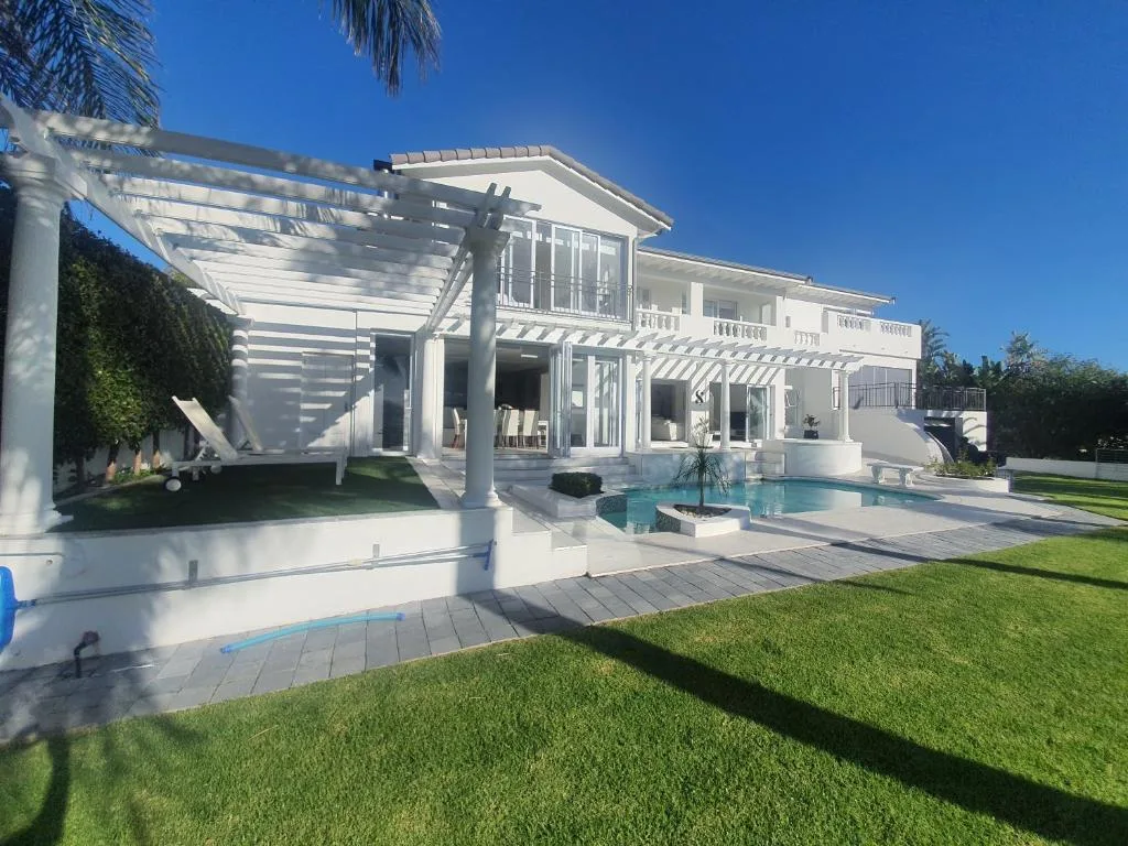 Modern white villa with pool, pergola, and manicured gardens under blue sky