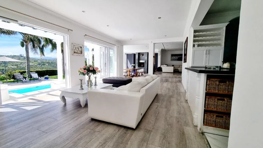Open-plan lounge with white sofa, pool view through glass doors, mountain backdrop