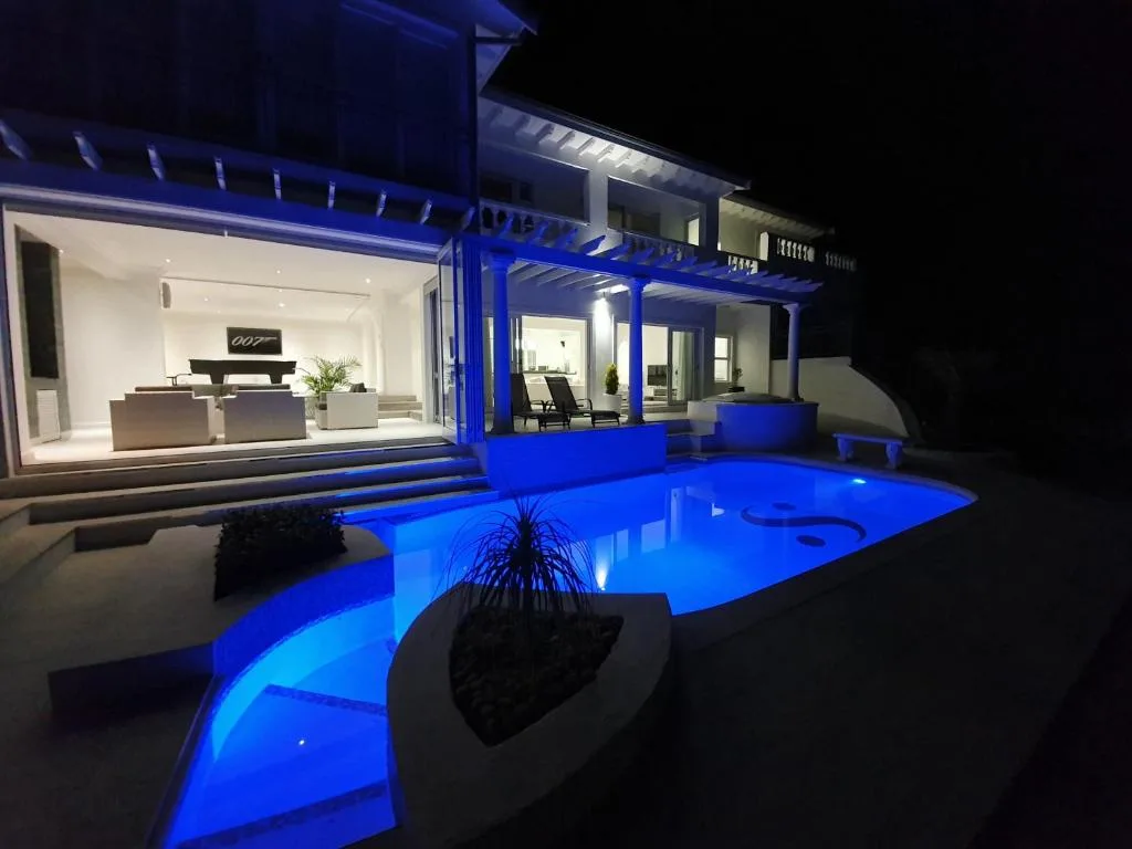 Illuminated swimming pool at night with modern house and deck lighting