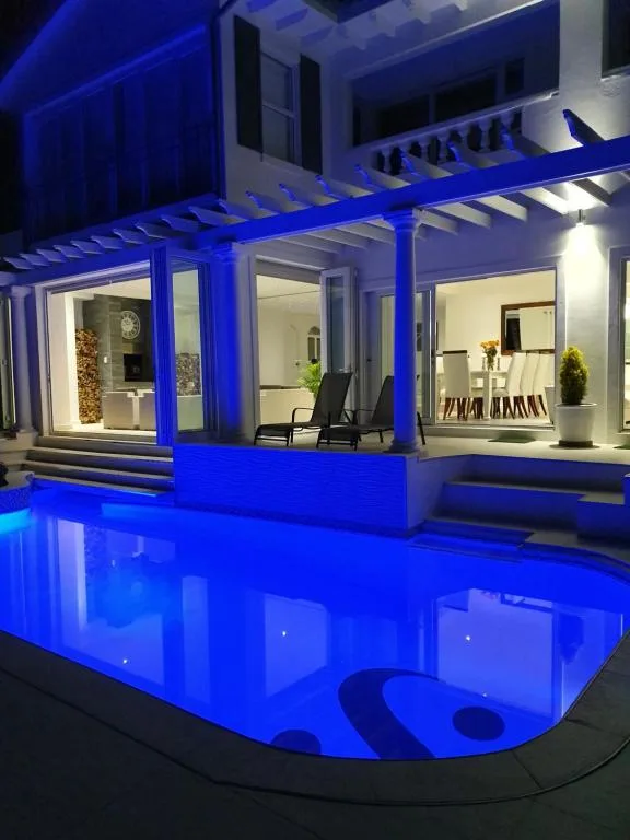 Illuminated swimming pool at night with modern house and dining area visible
