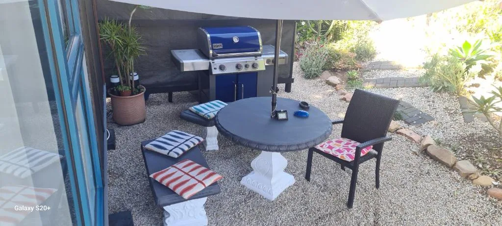 Outdoor braai area with blue gas grill, round table, and seating chairs
