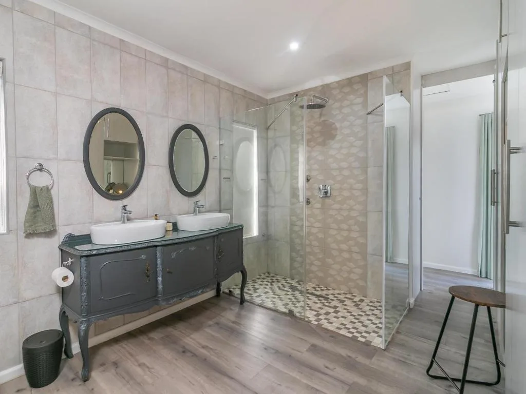 Modern bathroom with dual vanity sinks, round mirrors, and walk-in shower enclosure